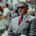Silvester Stallone sitzt in einem grauen Anzug und Sonnnbrille in einem Kaffee