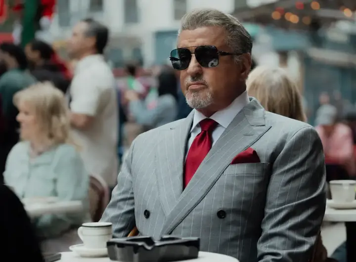 Silvester Stallone sitzt in einem grauen Anzug und Sonnnbrille in einem Kaffee