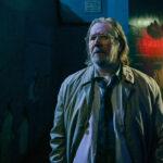 Gary Oldman steht in einer dunklen Straße. Er hat lange haare und sieht etwas fertig aus.